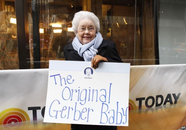 Ann Turner Cook holding a sign that says, The Original Gerber Baby