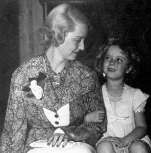 Bette Davis sitting with a young Shirley Temple. 