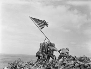 Ira Hayes stands on the left with arms outstretched to hoist the American flag upright