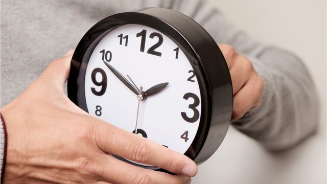 person adjusting a clock 1 hour backwards for 2019 fall daylight savings time