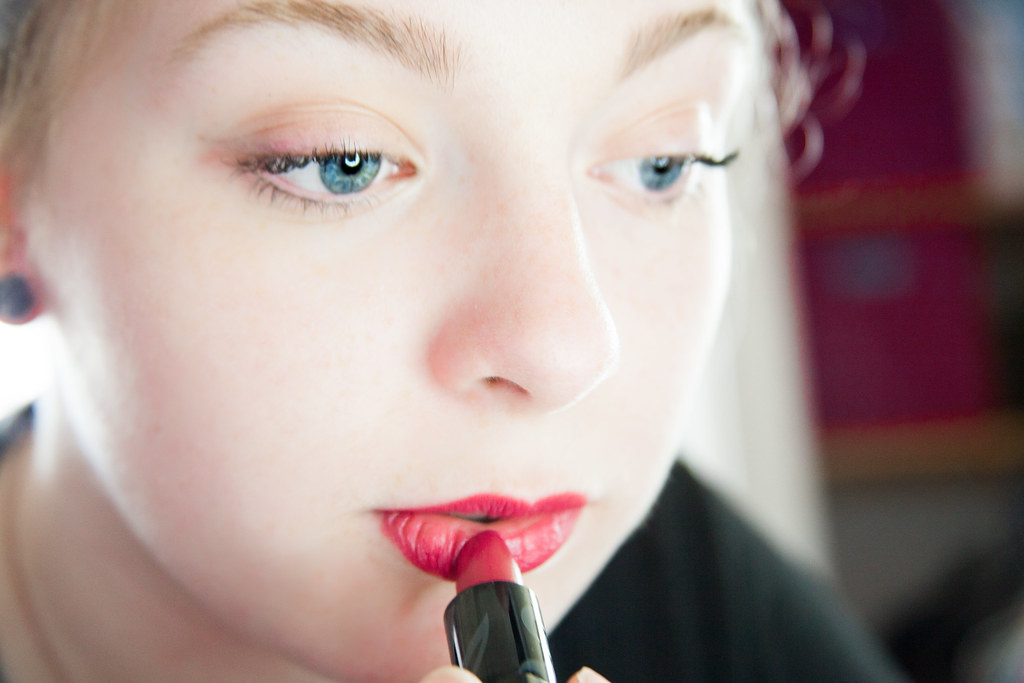 woman putting on red lipstick 