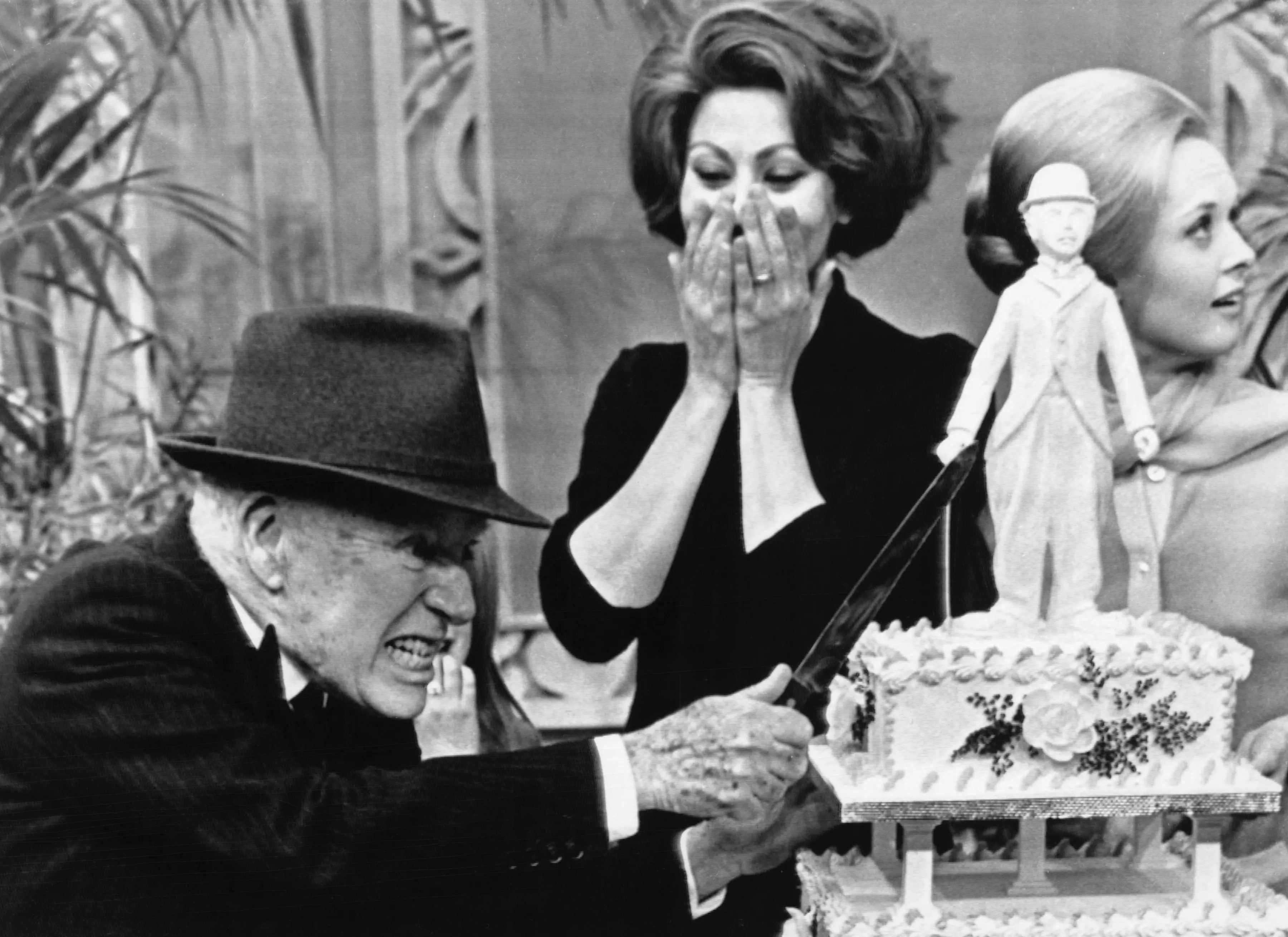 Charlie Chaplin attacks his birthday cake while Sophia Loren and Tippi Hedren watch