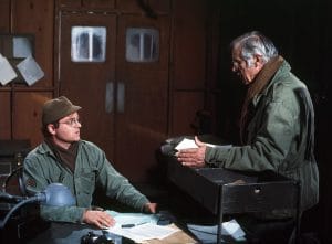 Gary Burghoff as Radar, left, hiding his left hand behind a table