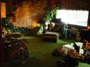 Graceland’s Jungle Room with green shag carpet, wood-paneled walls, tropical furniture, and animal-themed decor.