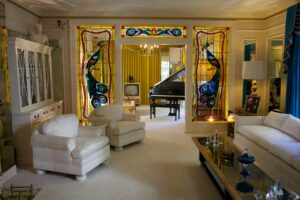 Graceland mansion living room featuring white sofas, ornate decor, a grand piano, and vintage 1970s styling.